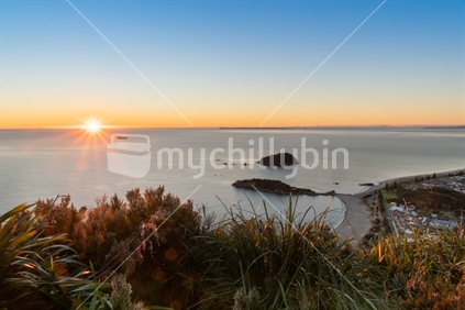 Ocean sunrise lens flare on horizon and lower slopes of Mount Maunganui, Tauranga