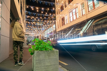 AUCKLAND, NEW ZEALAND - SEPTEMBER 14 2018; Auckland's Britomart area, bright and decorative lights, street furniture with blurred image of young fashionable woman walking along street at night