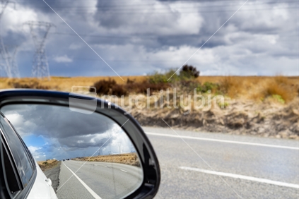 Driving State Highway 1 along Desert Road in middle New Zealand North Island looking forward and in  vehicle mirror rear vision high country landscape and passing power pylons