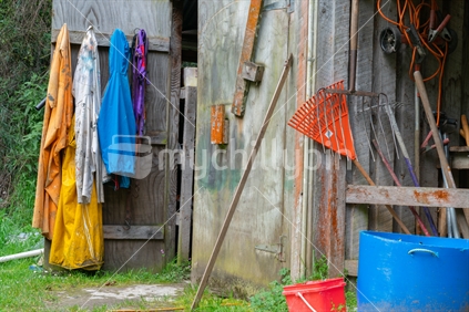Old shed open door with equipment and wet weather clothing hanging on door and typical farming paraphenalia