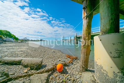 Waimea Estuary with old chain and orange buoy lying under wharf above low tide at Mapua South Island New Zealand.