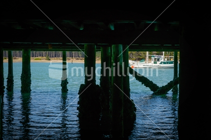 From shade to bright boat moored in channel looking from underneath wharf at Mapua on Tasman Bay in South Island New Zealand.