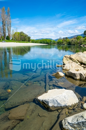Lime green spring growth of willow leaves along banks of scenic South Island's Takaka  River calm with reflections from surrounding trees.