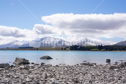 Ruataniwha Inlet foreshore at low tide with snow on top distant mountains under dramaitc clouds at Collingwood, Tasman Bay New Zealand.