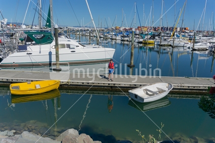 Small boy off marina pier fishing with moored boats background