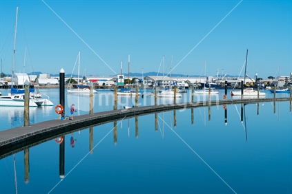 Long curving pier surrounded by blue calm water with small boy in red life jacket fishing in distance at Tauranga New Zealand.