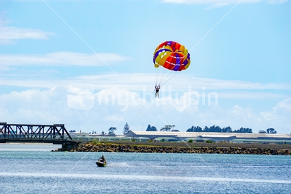 TAURANGA, NEW ZEALAND DECEMBER 22 2018; Summer fun, being towed over the bay while hanging under a para-glider with bright coloured canopy.