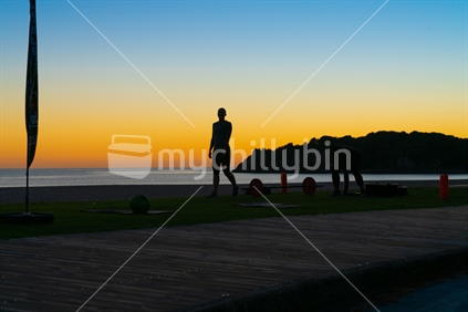 People on beach at Mount Maunganui at sunrise in silhouette doing morning fitness exercise.