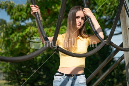 Teenage girl in children's playground holding black climbing tubular equipment at Tauranga Domain, New Zealand.