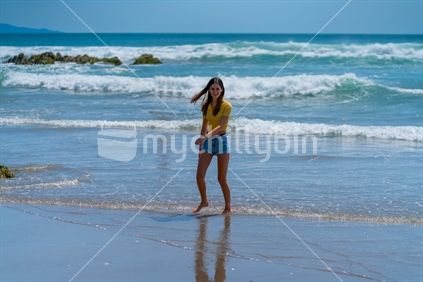 Teenager on beach with sea and waves in background, Mount Maunganui, New Zealand.