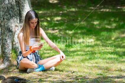 Teenage girl sitting in McLaren Falls Park looking at her mobile phone.