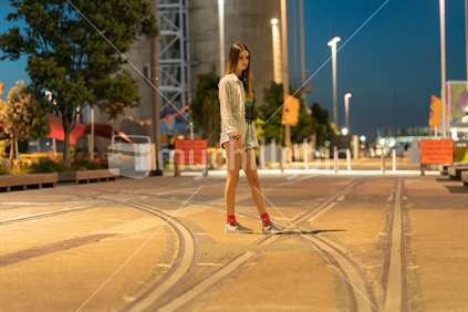 Teenager walking across old railway tracks with industrial background at night.  Nice head movement slight motion blur.