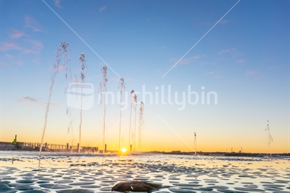 Water feature with spraying water on Tauranga Strand waterfront at sunrise with clear blue sky, New Zealand