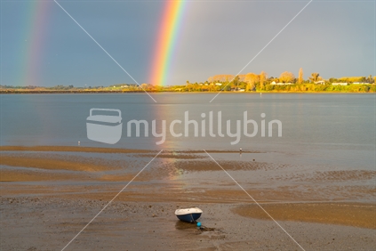 Rainbow falls to horizon then reflects across bay to dinghy sitting on beach.