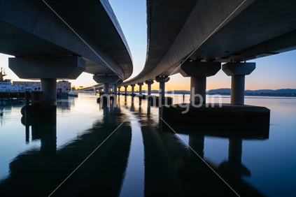 Curving lines and reflections on calm water under Tauranga Harbour Bridge.
