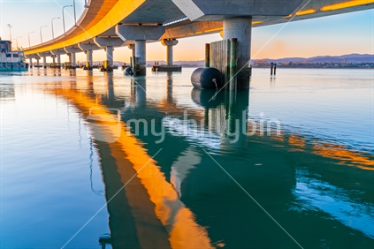 Curving lines and reflections on calm water under Tauranga Harbour Bridge.