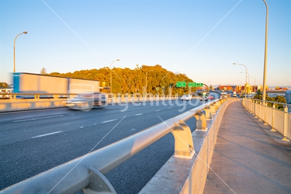 Early sun casts golden glow over Tauranga Harbour Bridge as business day starts and traffic builds up blurred in motion.