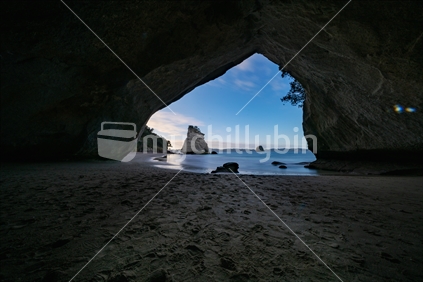 Te Hoho Rock standing in sun framed by tsilhouette of natural arch of Cathedral Cove on Coromandel Peninsula New Zealand.