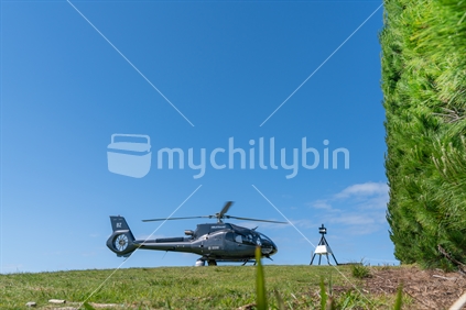 Waiheke Island Auckland New Zealand - October 2 2020; Black helicopter landed on hilltop by black and white trig.
