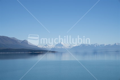 shoreline and view across  calm Lake Pukaki with Mount Cook and Southern Alps in distance.