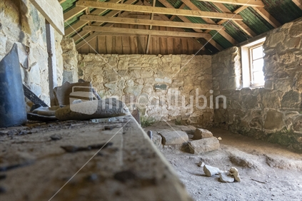 Interior of historic Ackers stone cottage on Stewart Island. showing, beams, stone walls and general clutter.