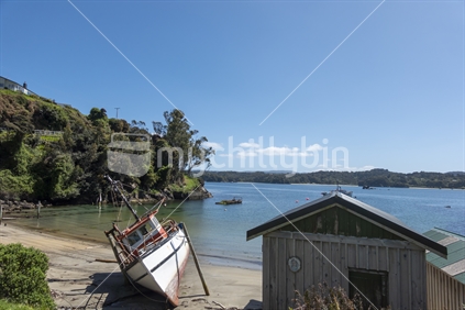 Leask Bay beach and boat sheds with beached old boat lying on sand on Sterwart Island, New Zealand.