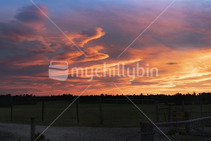 Dramatic bright colourful sunset sky over silhouette rural landscape in South Island New Zealand.