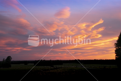 Dramatic bright colourful sunset sky over silhouette rural landscape in South Island New Zealand.