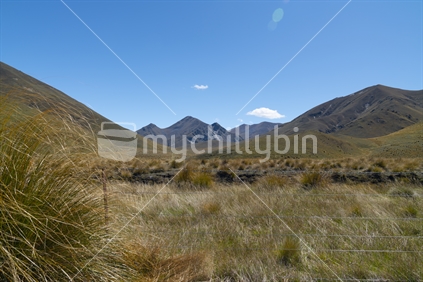 lens flare in blue sky between peaks and over tussock covered valleys of Lindis Pass, famous road trip Central Otago New Zealand.