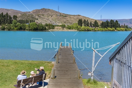 Cromwell New Zealand -  November 10 2020; Grandparents sit with child by wooden pier into turquoise Kawarau River at historic precint in town.