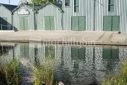 Christchurch New Zealand - November 21 2020; Closed doors of row of green boatsheds along and reflected in Avon River in the city
