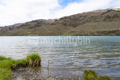 River banks flowing water and hills on other side of scenic Clutha River in Central Otago, New zealand.