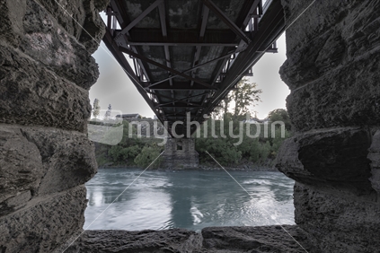 Through stone piers of Earnscleugh Bridge in early morning light as little mist rises from Clutha River Cromwell in Central Otaog New Zealand.
