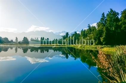 Reflections in Lake Matheson surrounded by natural bush and forest and Southern Alps mountain range in South Island New Zealand.