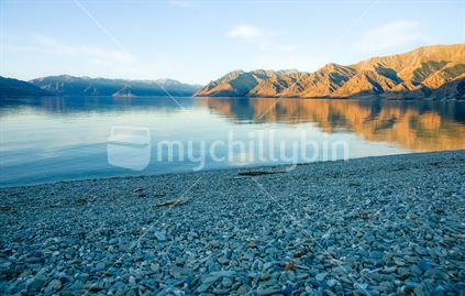 Peaceful Lake Wanaka in morning light surrounding hills and blue sky.