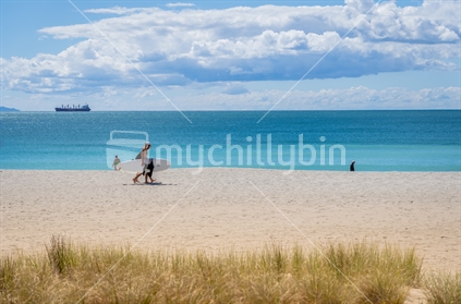 Tauranga New Zealand - March 22 2023: Mount Maunganui Main Beach background scene with people walking carrying surfboard.