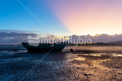 As the sunrises a dinghy is silhouetted at a bay at low tide.