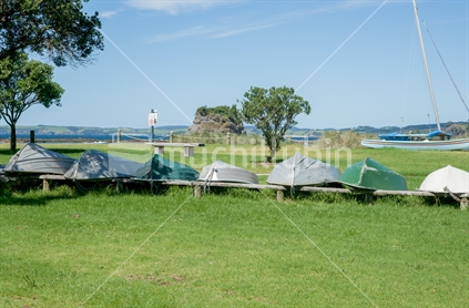 Dinghies upturned on grass near beach surrounded by trees in Northland New Zealand.