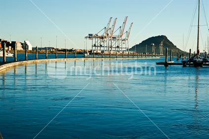 Bright blues of harbour and sky just after sunrise, with industrial scene, port cranes and Mount Maunganui.