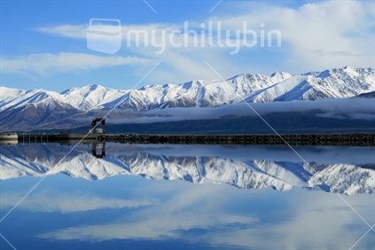 Range of snowy mountains overlooking a salmon farm in the South Island