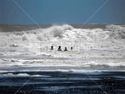 Teens enjoying a swim in the foamy water at the beach in Mokau