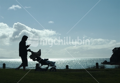 Silhouette of man texting and walking the baby beside a beach; Tauranga, New Zealand.