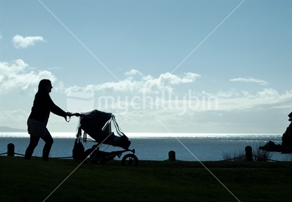 Silhouette of woman walking a baby beside a beach; Tauranga, New Zealand.