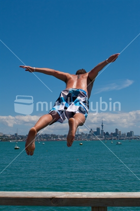 Man jumps into the water near Devonport, with Auckland CBD and Skytower in the background