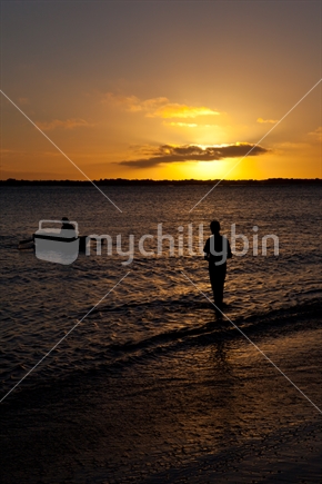 Boy waiting for his dad to reach shore at dusk, Northland, New Zealand