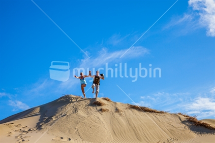 Young couple having fun and jumping off a sand dune