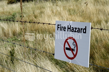 A Fire hazard warning sign, tied to a barbed wire  boundary fence 