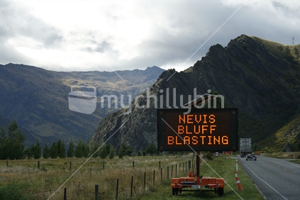 Traffic warning sign, while Nevis Bluff is blasted to remove loose rocks for safety.  Central Otago.