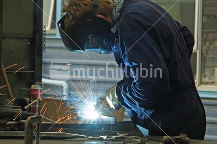 A tradesman, welding metal in an engineering workshop.