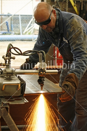 A tradesman, using a gas cutter to cut  a  metal plate in an engineering workshop.